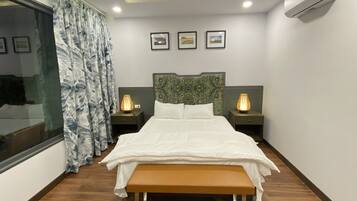 A modern bedroom with a large bed, two bedside tables with lamps, a bench, a window with curtains, and a ceiling fan.