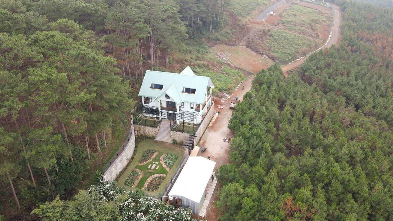 Luchtbeeld van een twee verdiepingen tellend huis, omringd door dicht bos, met een verharde oprit en een kleine tuin.