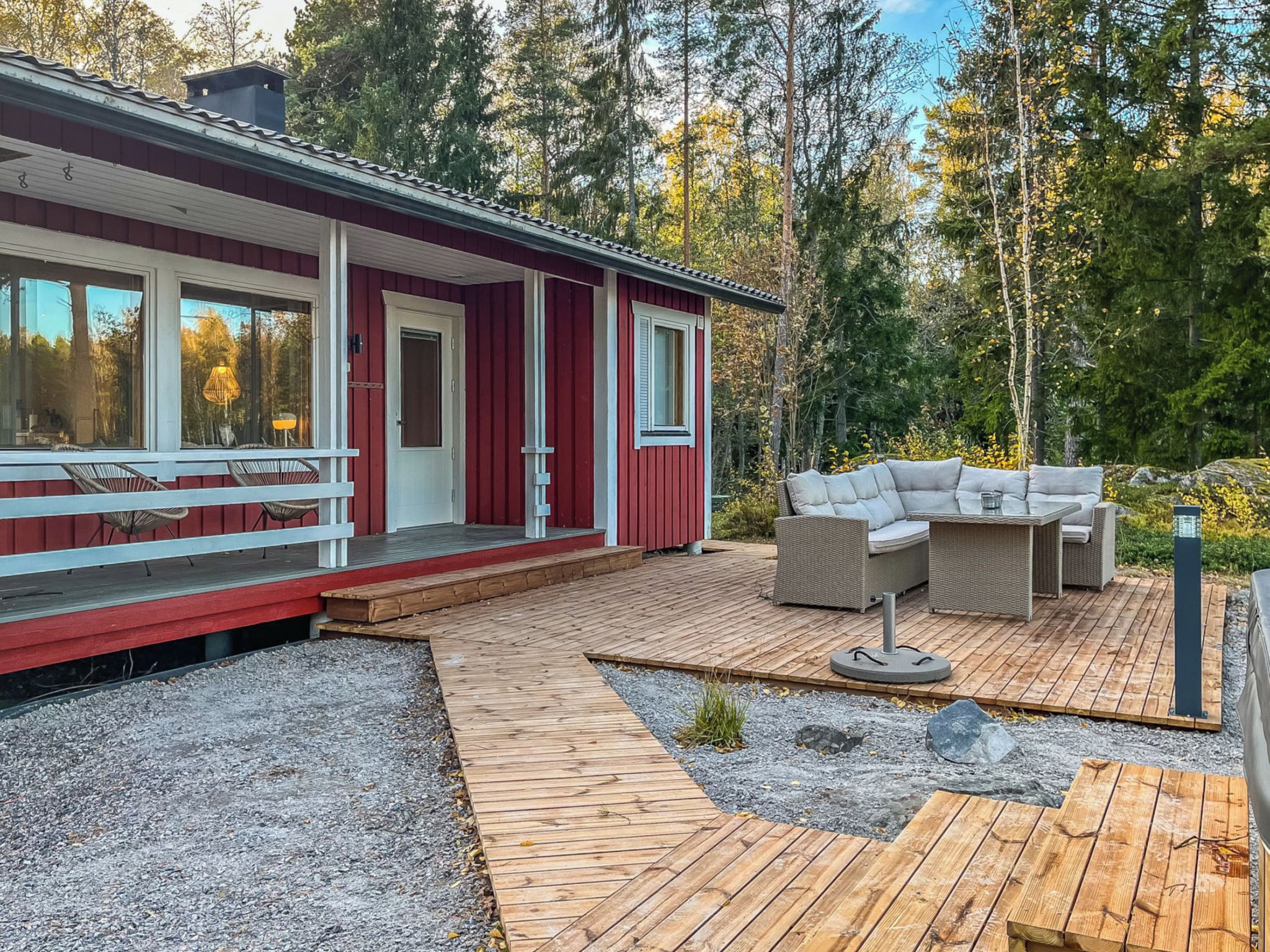 Uma cabana vermelha com um deck de madeira, móveis de exterior e um espaço com pedriscos.