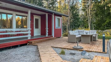 Uma cabana vermelha com um deck de madeira, móveis de exterior e um espaço com pedriscos.