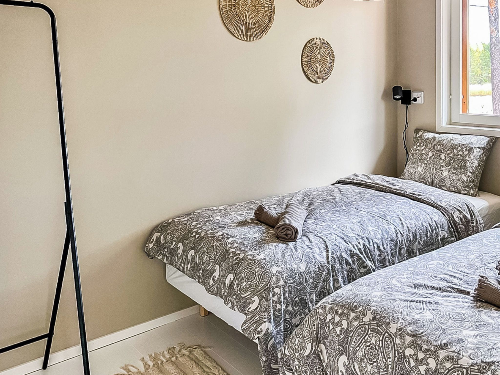 A bedroom with two beds, patterned bedding, a window with a view, and decorative wall art.