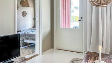 Une pièce avec un lit, un téléviseur posé sur un socle en pierre, une porte ornée d’un rideau rose et une bougie blanche sur une table en bois.