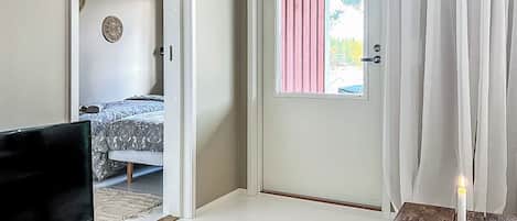Een kamer met een bed, een televisie op een stenen voetstuk, een deur met een roze gordijn en een witte kaars op een houten tafel.