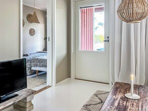A room with a bed, a television on a stone stand, a door with a pink curtain, and a white candle on a wooden table. - Villa havet by Interhome (Porvoo)