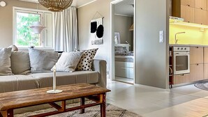 A modern living room with a sofa, a wooden coffee table, and a hanging light fixture. There is a kitchen area with wooden cabinets and a yellow countertop. - Villa havet by Interhome (Porvoo)