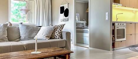 A modern living room with a sofa, a coffee table, and a kitchen area with cabinets and a stove.