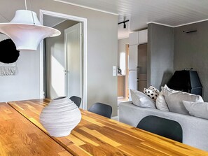 Un espacio habitable moderno con una mesa de comedor de madera, un florero blanco, un sofá gris con cojines estampados y una lámpara colgante blanca.