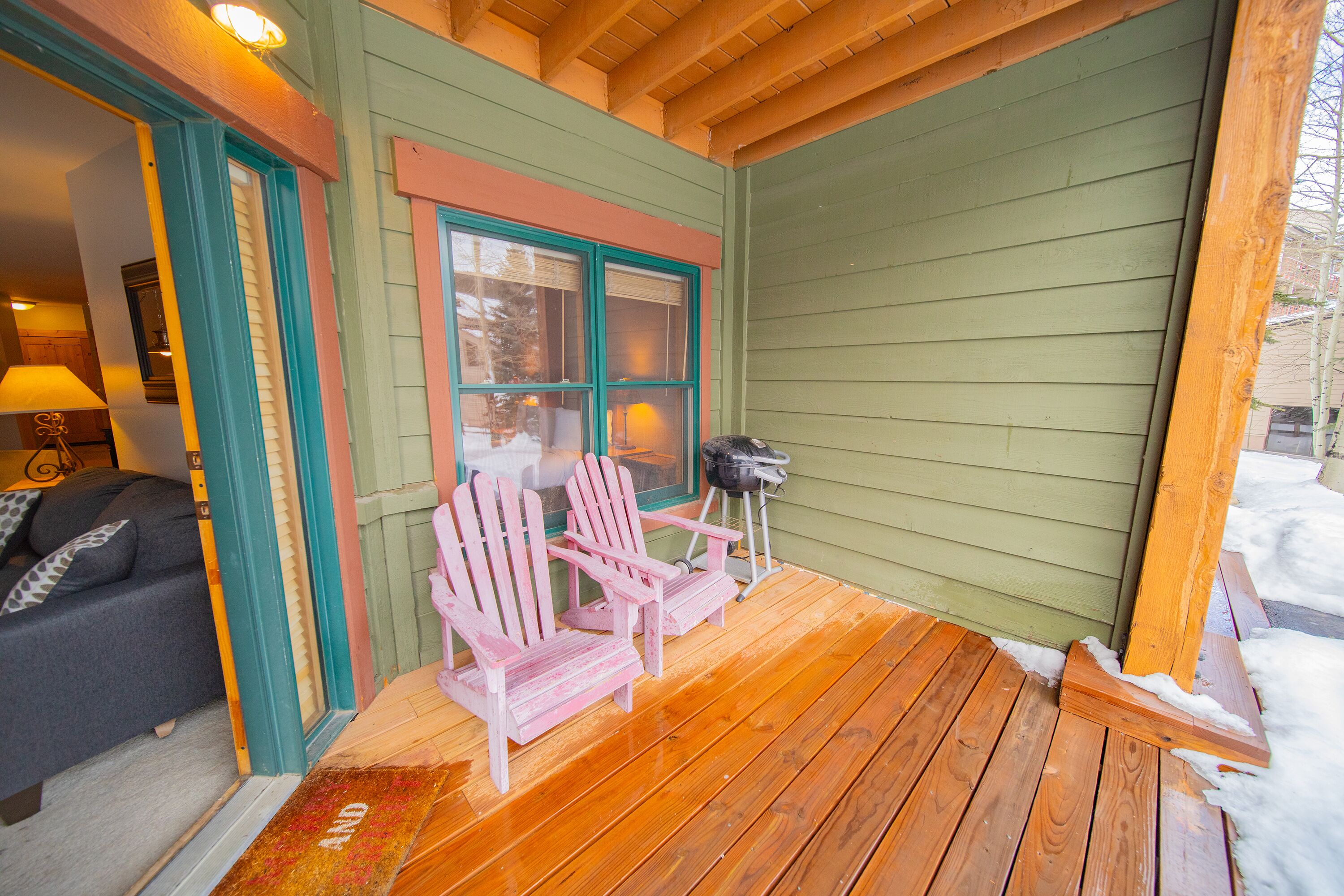 A wooden deck with two Adirondack chairs, a grill, and a green exterior wall.