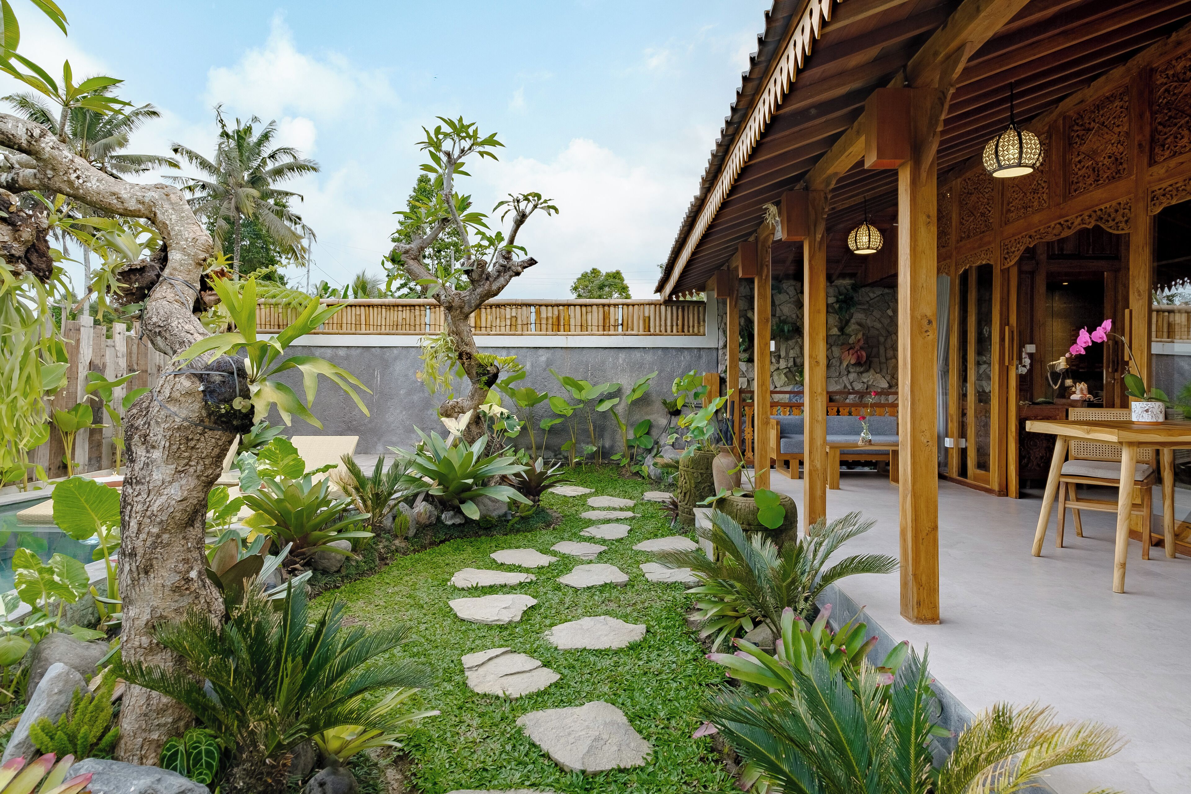 A traditional wooden building with a covered patio area, stone steps, and lush greenery.