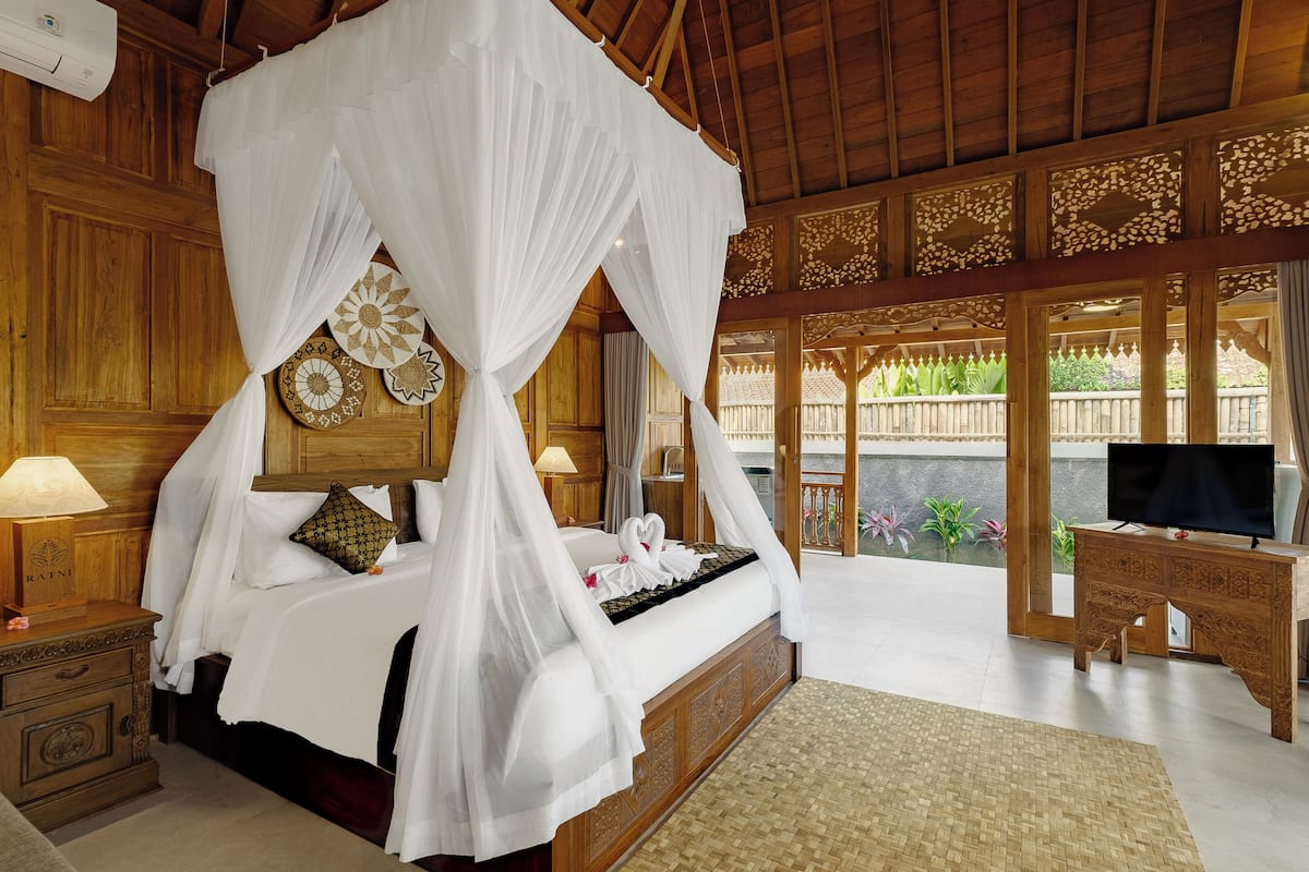 A four-poster canopy bed with a television and wooden desk in a room with wooden paneling and a balcony view.