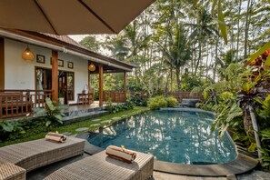 A pool area with lounge chairs, a covered seating area, and lush tropical vegetation. - Ratni Ubud Villa (Ubud)