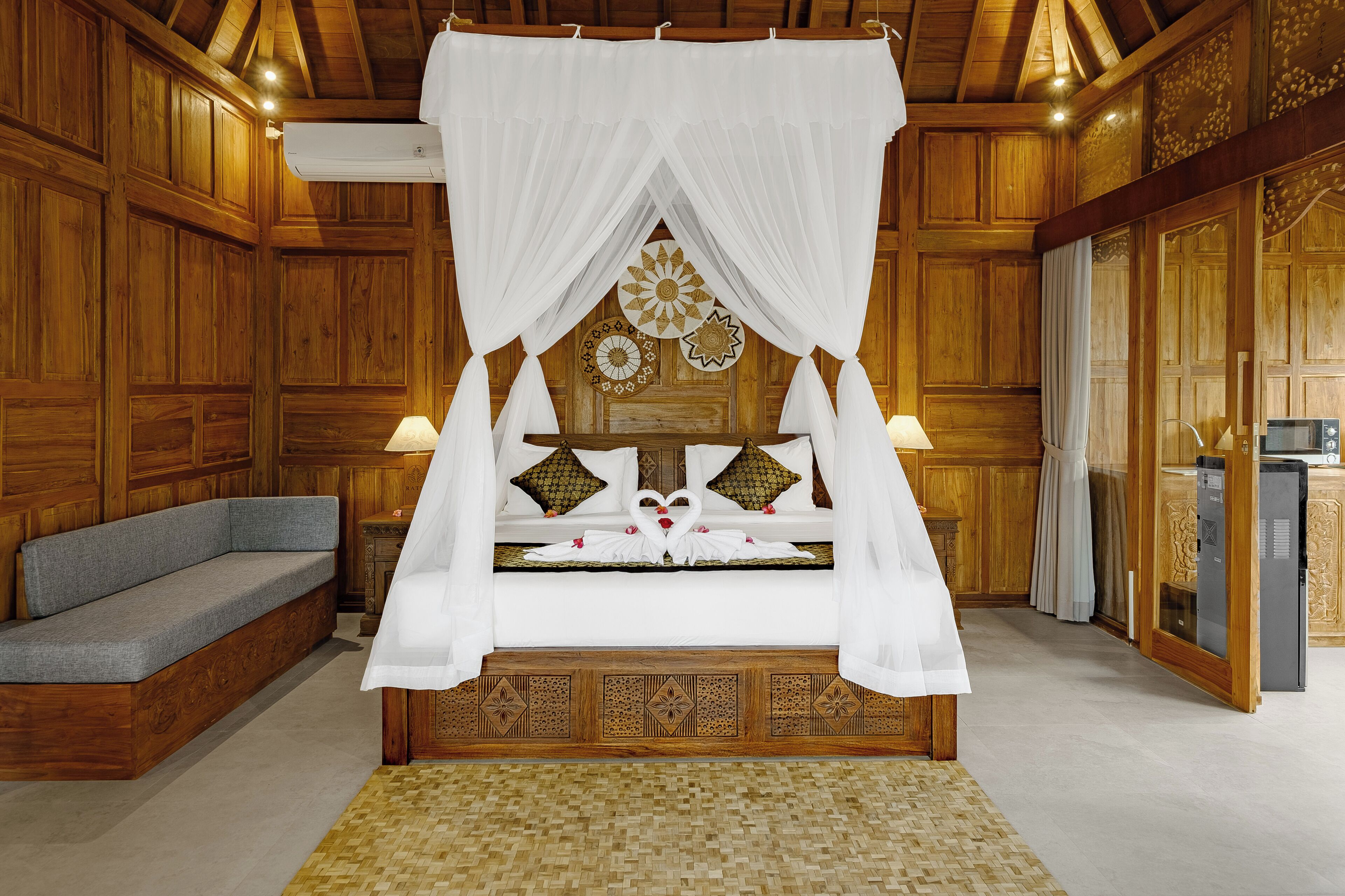 Una cama con dosel de madera con cortinas blancas, un sofá gris y una pequeña mesa con un objeto decorativo.