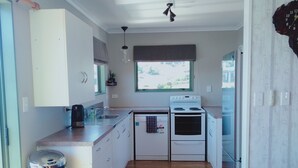 Una cuina moderna amb armaris blancs, un cubell de brossa d'acer inoxidable, una taula de dinar de fusta i una vista de l'exterior a través d'una finestra.