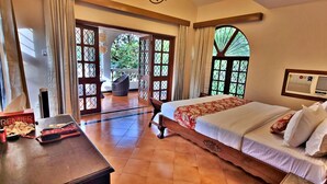 A bedroom with a large bed, a wooden headboard, and a view of a garden through open doors. - Luxury Vintage Villa in the heart of North Goa. (Verla Canca)