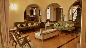 A spacious living room with a green sofa, wooden coffee table, and a dining area with chairs and a table. - Luxury Vintage Villa in the heart of North Goa. (Verla Canca)