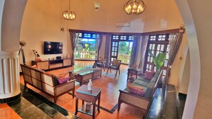 A spacious lobby with a high ceiling, a central seating area with sofas and chairs, a television mounted on the wall, and a large window providing a view of the outdoors. - Luxury Vintage Villa in the heart of North Goa. (Verla Canca)