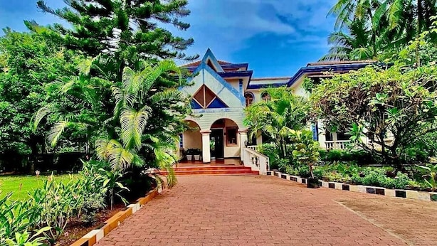 A building with a central entrance, surrounded by lush greenery and a paved pathway leading to it. - Luxury Vintage Villa in the heart of North Goa. (Verla Canca)