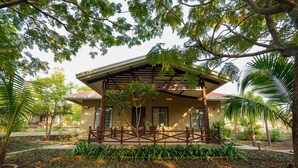 A building with a covered porch, surrounded by lush greenery and palm trees.