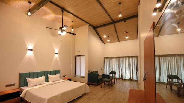 A spacious bedroom with a large bed, a desk, and a chair. There is a ceiling fan and multiple light fixtures.