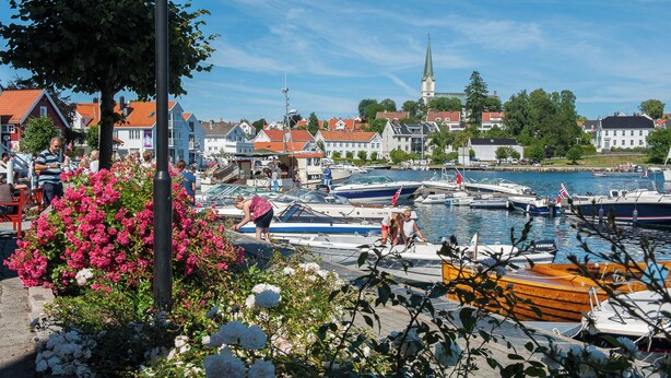 A harbor with boats docked, a church in the background, and a row of houses. - Vertikalen (Lillesand)