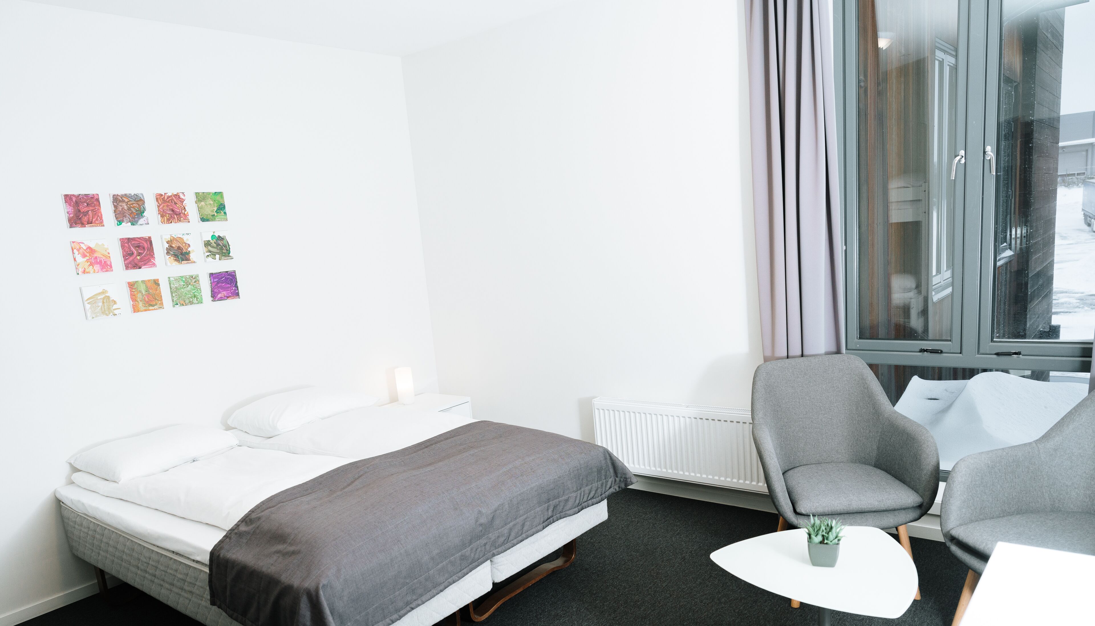 Ein Hotelzimmer mit Bett, zwei Stühlen, einem kleinen Tisch und einem Fenster mit Vorhängen.