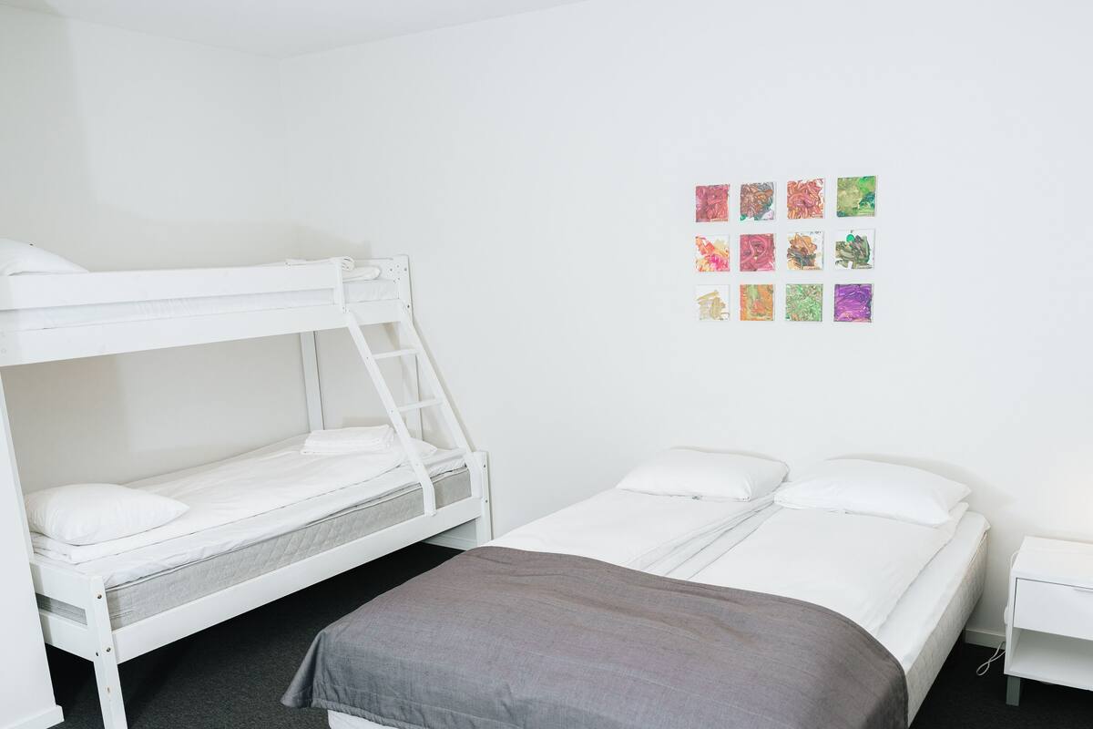 A bunk bed room with a lower bunk, a single bed, and a nightstand with a lamp.