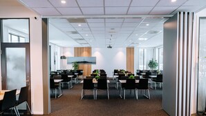 A spacious conference room with multiple tables and chairs, large windows, and a modern ceiling design. - Vertikalen (Lillesand)