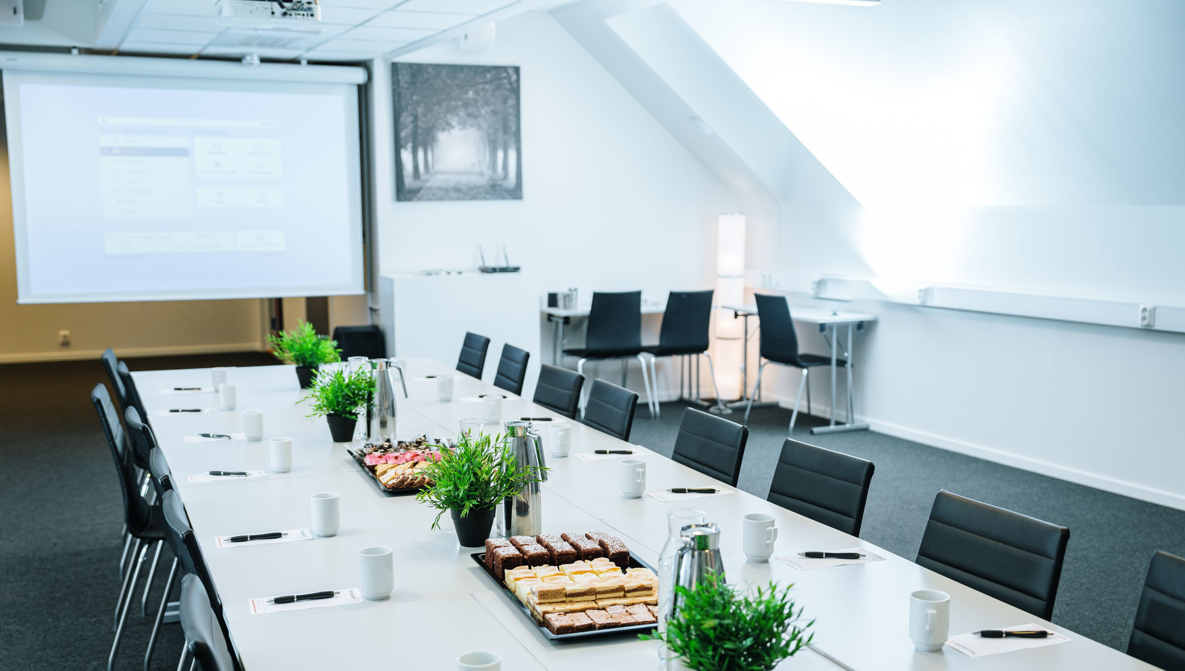 Ett konferensrum med ett långt bord, stolar, en projektorduk och en presentation på väggen.