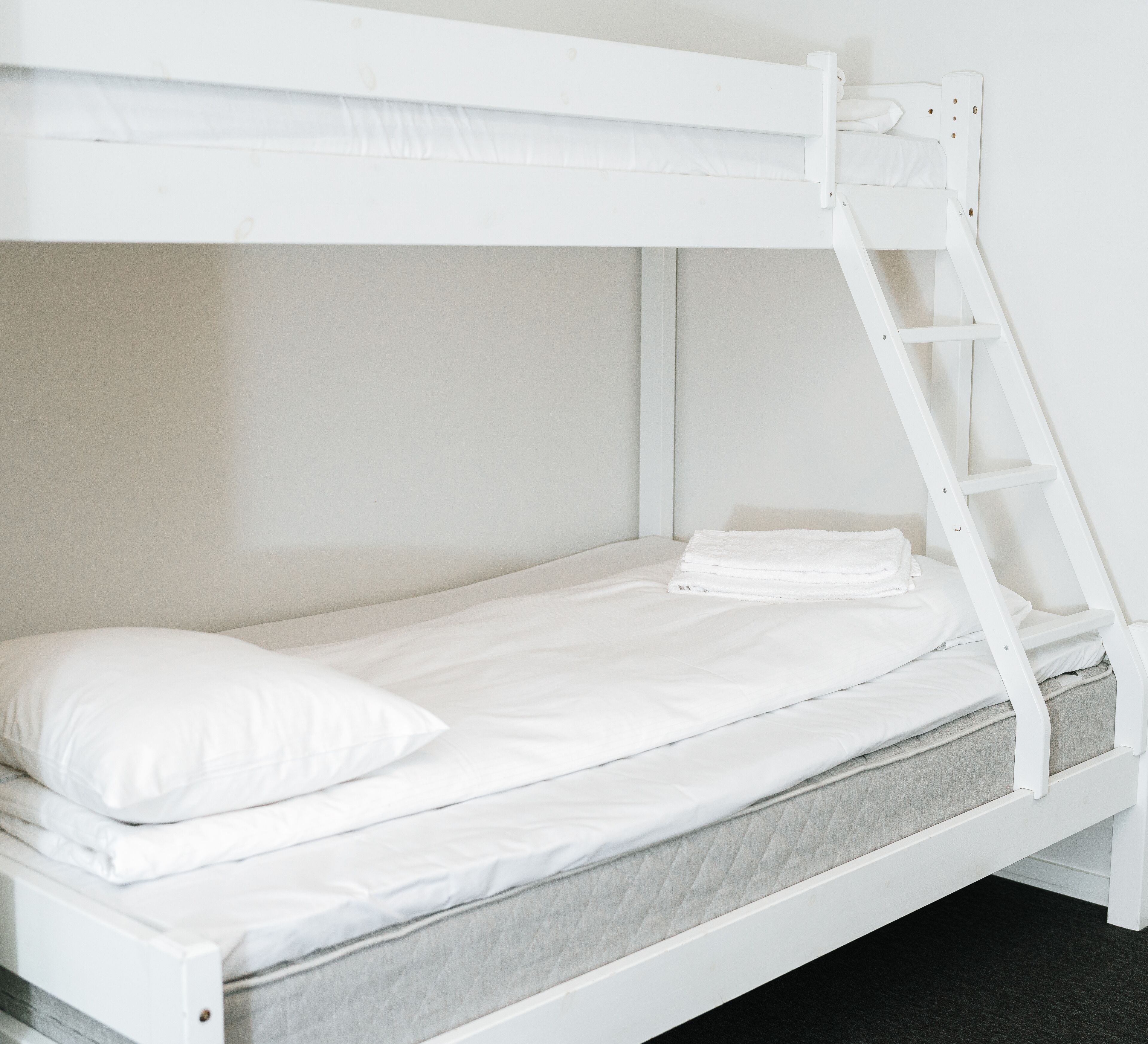 Una cama litera con escalera, ropa de cama blanca y colchón gris.