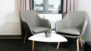 A modern room with two grey armchairs, a white table, and a window with curtains. - Vertikalen (Lillesand)