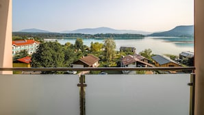 A view from a balcony overlooking a lake with mountains in the background, houses with red roofs, and a clear sky. - Faaker See Inn (Finkenstein am Faaker See)