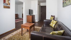 A living room with a leather sofa, a wooden coffee table, a television on a wooden cabinet, and a large painting on the wall. - Faaker See Inn (Finkenstein am Faaker See)