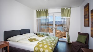 A bedroom with a bed, a chair, a table, and a window with curtains. - Faaker See Inn (Finkenstein am Faaker See)