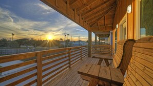 A wooden deck with benches and a railing overlooking a sunset. - Pool, Boat Dock, Balcony w/ Bay Views | Cooper's Hawk by AvantStay (Corpus Christi)