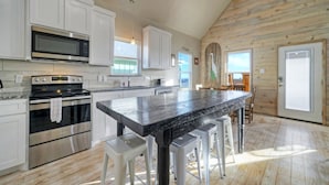 A modern kitchen with stainless steel appliances, a large island with stools, and wooden flooring. - Pool, Boat Dock, Balcony w/ Bay Views | Cooper's Hawk by AvantStay (Corpus Christi)