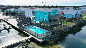 A waterfront property with a swimming pool, multiple decks, and a pier. - Pool, Boat Dock, Balcony w/ Bay Views | Cooper's Hawk by AvantStay (Corpus Christi)