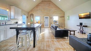 A spacious kitchen with a wooden ceiling, a dining area with a bench, and a living room with a sofa. - Pool, Boat Dock, Balcony w/ Bay Views | Cooper's Hawk by AvantStay (Corpus Christi)