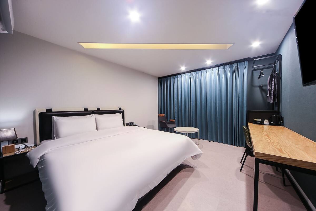 Une chambre d’hôtel moderne équipée d’un grand lit, d’un bureau, d’une chaise, d’une petite table et d’un téléviseur fixé au mur.