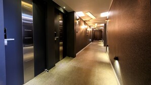 A modern hotel corridor with a long, narrow hallway, recessed lighting, and a textured wall on one side. - ONNA HOTEL (Busan)
