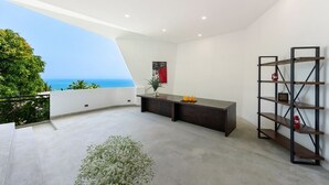 Un intérieur moderne avec un balcon donnant sur la mer, un bureau en bois foncé et une étagère en métal.