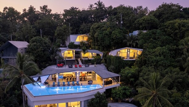 Une maison moderne à plusieurs étages, dotée d’une piscine sur le toit et entourée d’une végétation luxuriante.