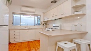 Una cocina moderna con armarios blancos, suelo de madera, una ventana y una pequeña barra con taburetes.