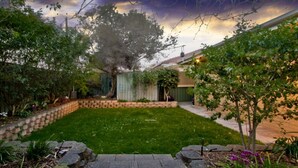 Un jardín bien cuidado con césped, un camino de ladrillo y un gran árbol.