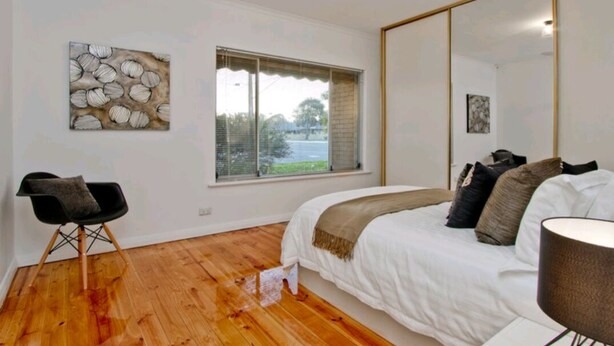 Un dormitorio con una cama grande, una ventana con persianas, una silla y un cuadro en la pared.