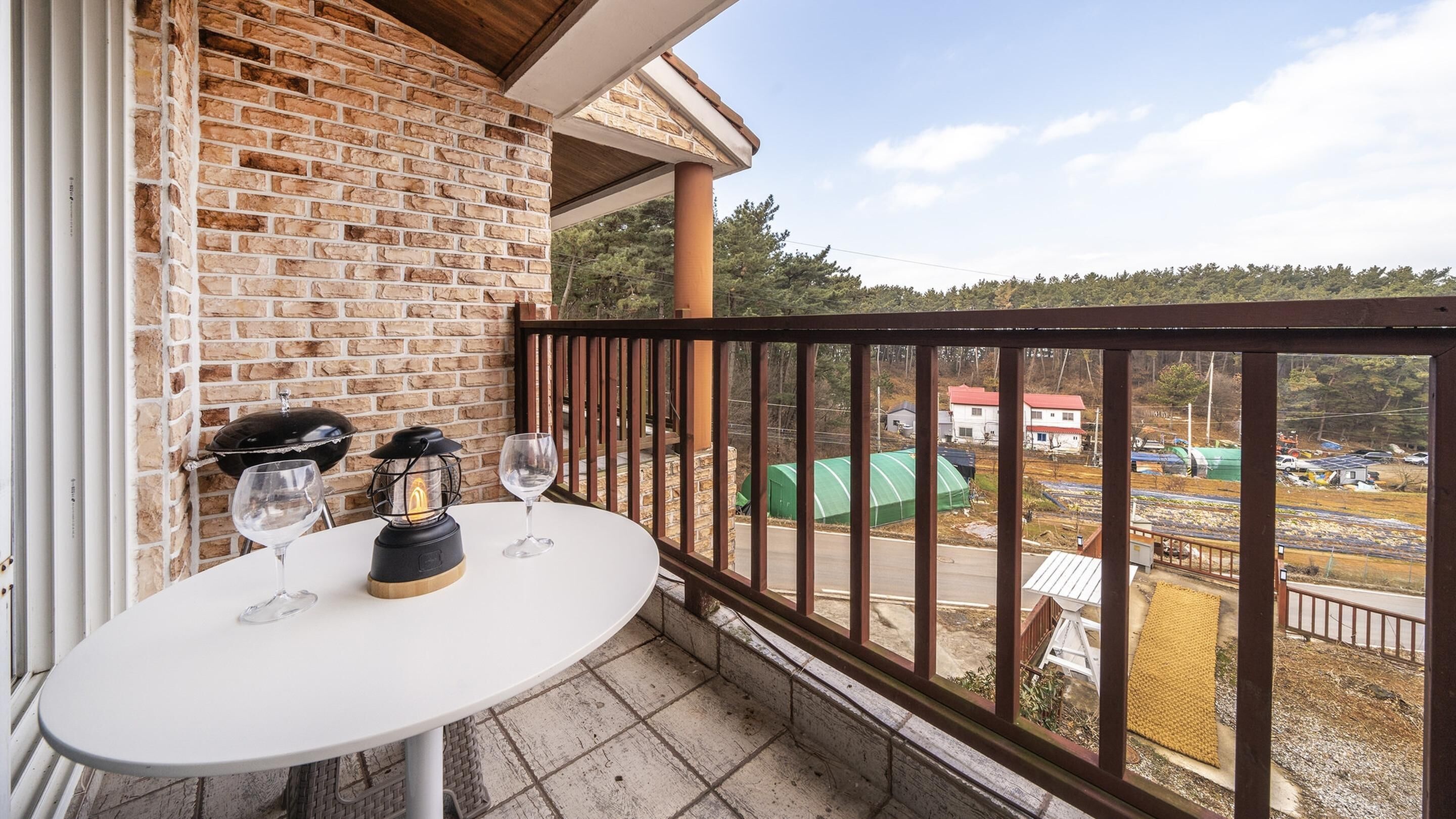 A balcony with a brick wall, a white table, two wine glasses, and a lantern.