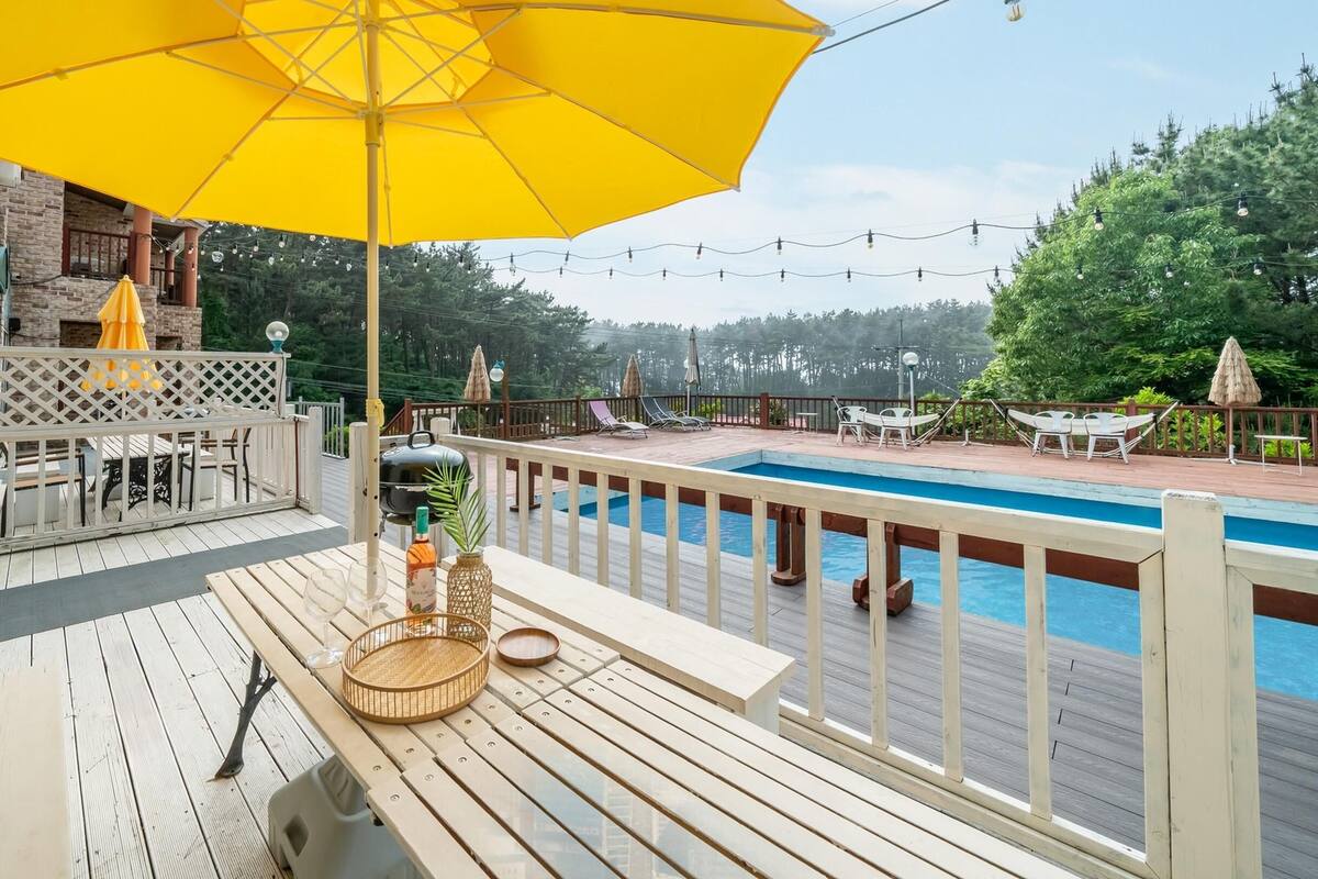 A wooden deck with a pool, outdoor furniture, and a yellow umbrella.