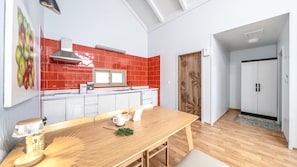 Une cuisine moderne avec des carreaux rouges, des armoires blanches et une table à manger en bois, accompagnée de chaises.