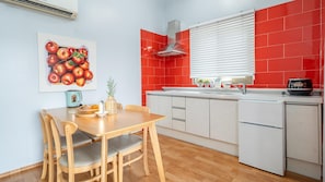 Une cuisine moderne avec des carreaux rouges et blancs, une table à manger en bois avec des chaises, une machine à café et un panier de fruits.