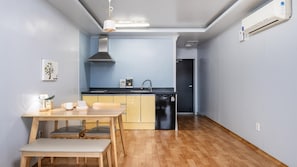 Une cuisine compacte avec un coin repas, comprenant une table en bois, des chaises, un lave-vaisselle noir et une cuisinière encastrée.