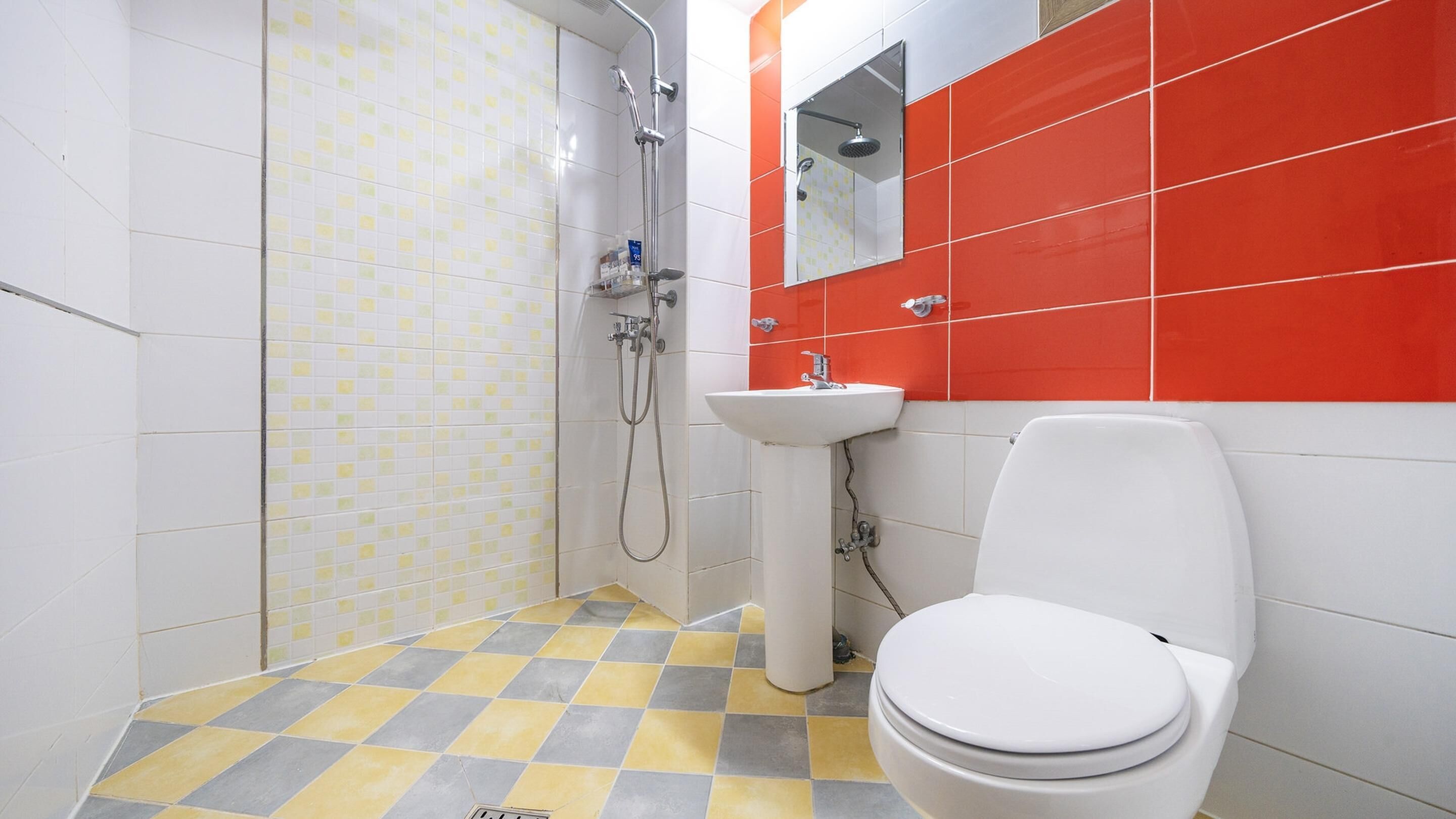 Un baño con inodoro blanco, lavamanos y ducha. El suelo presenta un estampado de cuadros amarillos y grises.